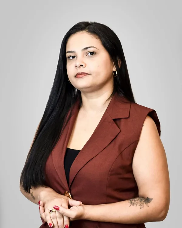 Priscila Horácio Nunes de colete bordô, em pé, fundo cinza